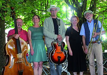 Eine Band mit ihren Instrumenten, darunter Bass und eGittarre, steht vor mehreren Bäumen