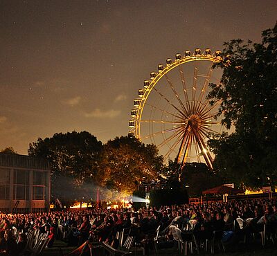 Viele Personen auf Stühlen bei der swa Kurzfilmnacht 2024. Im Hintergrund sind Bäume und ein Riesenrad